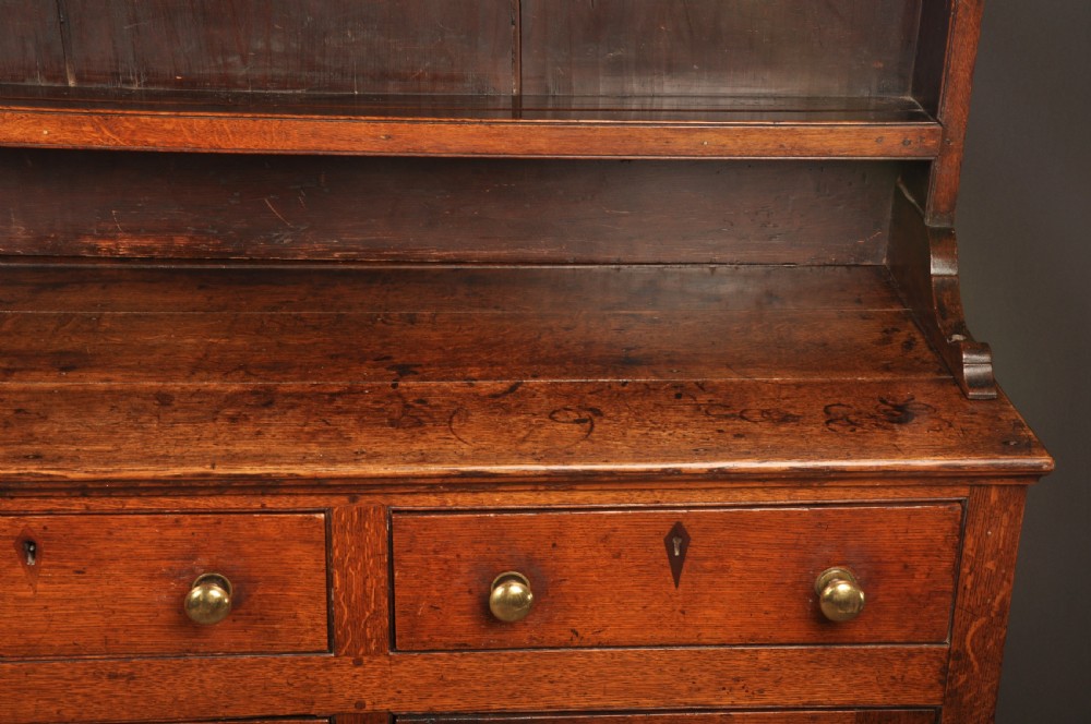 An eighteenth-century warm brown oak dresser featuring an upper three-tier open plate rack above a lower cabinet with drawers and panelled cupboard doors. View V
