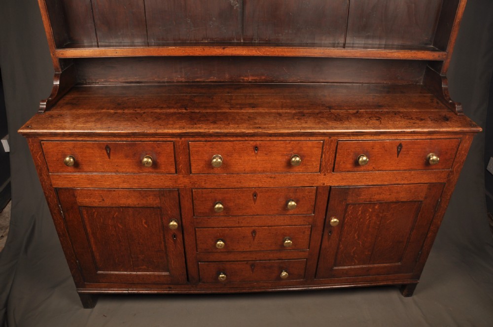 An eighteenth-century warm brown oak dresser featuring an upper three-tier open plate rack above a lower cabinet with drawers and panelled cupboard doors. View VI