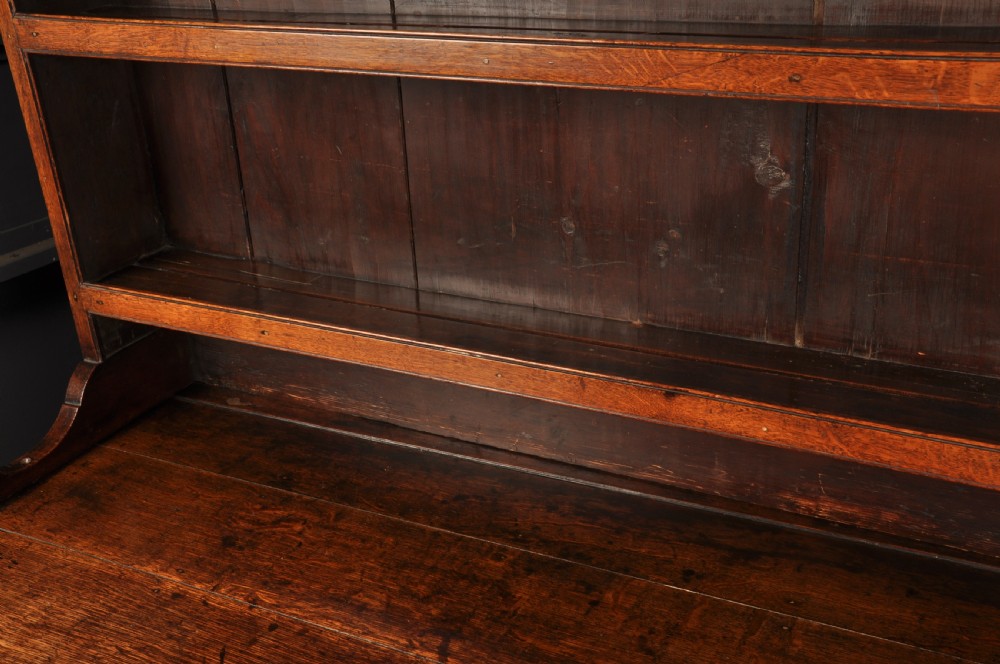 An eighteenth-century warm brown oak dresser featuring an upper three-tier open plate rack above a lower cabinet with drawers and panelled cupboard doors. View VII