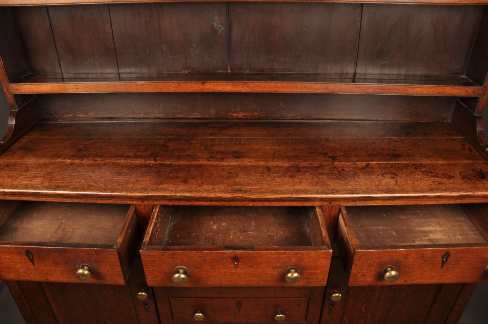 An eighteenth-century warm brown oak dresser featuring an upper three-tier open plate rack above a lower cabinet with drawers and panelled cupboard doors. View VIII