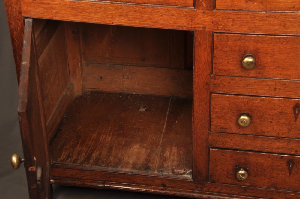 An eighteenth-century warm brown oak dresser featuring an upper three-tier open plate rack above a lower cabinet with drawers and panelled cupboard doors. View X