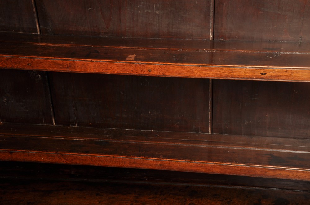 An eighteenth-century warm brown oak dresser featuring an upper three-tier open plate rack above a lower cabinet with drawers and panelled cupboard doors. View XII