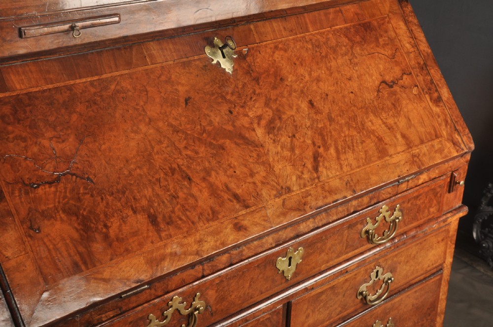 A George I burr walnut bureau bookcase with double mirrored upper doors over a slant-front slope and chest of drawers with brass handles. View II