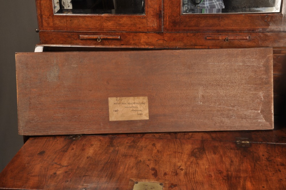 A George I burr walnut bureau bookcase with double mirrored upper doors over a slant-front slope and chest of drawers with brass handles. View III