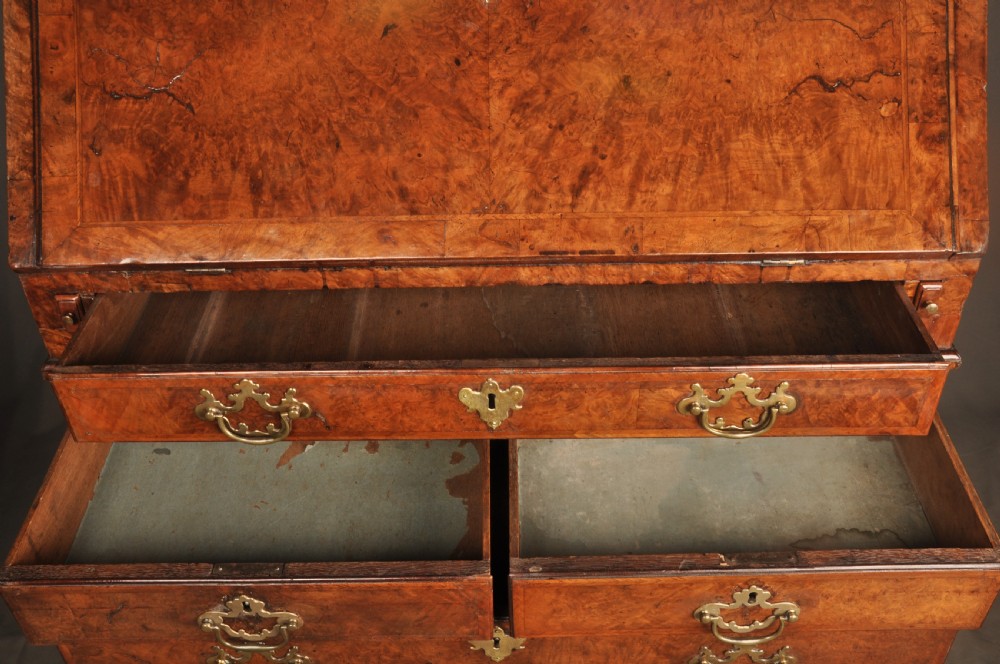 A George I burr walnut bureau bookcase with double mirrored upper doors over a slant-front slope and chest of drawers with brass handles. View VII