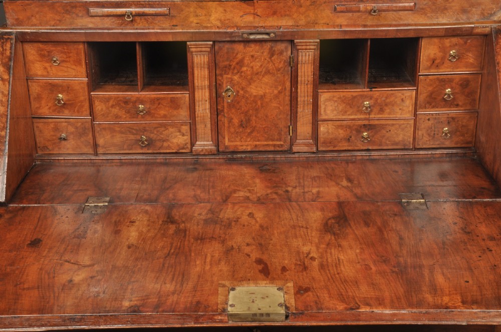 A George I burr walnut bureau bookcase with double mirrored upper doors over a slant-front slope and chest of drawers with brass handles. View VIII