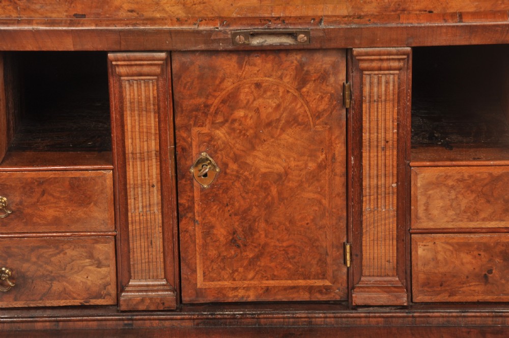 A George I burr walnut bureau bookcase with double mirrored upper doors over a slant-front slope and chest of drawers with brass handles. View IX