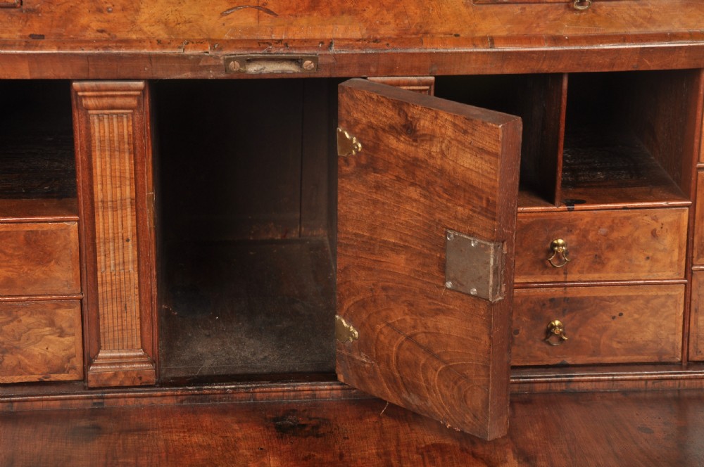 A George I burr walnut bureau bookcase with double mirrored upper doors over a slant-front slope and chest of drawers with brass handles. View X