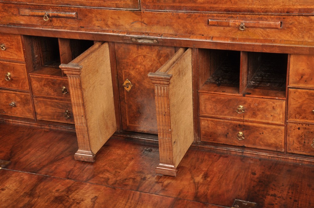 A George I burr walnut bureau bookcase with double mirrored upper doors over a slant-front slope and chest of drawers with brass handles. View XI
