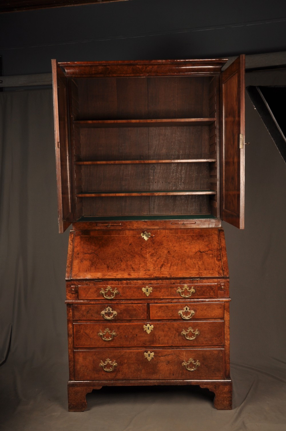 A George I burr walnut bureau bookcase with double mirrored upper doors over a slant-front slope and chest of drawers with brass handles. View XVIII