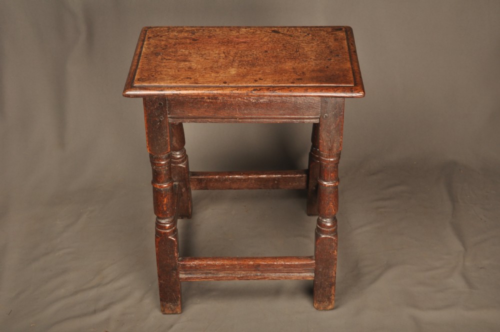 An 18th-century oak joint stool featuring baluster turned legs, plain stretchers, a rectangular moulded top, and dark brown patinated wood. View II