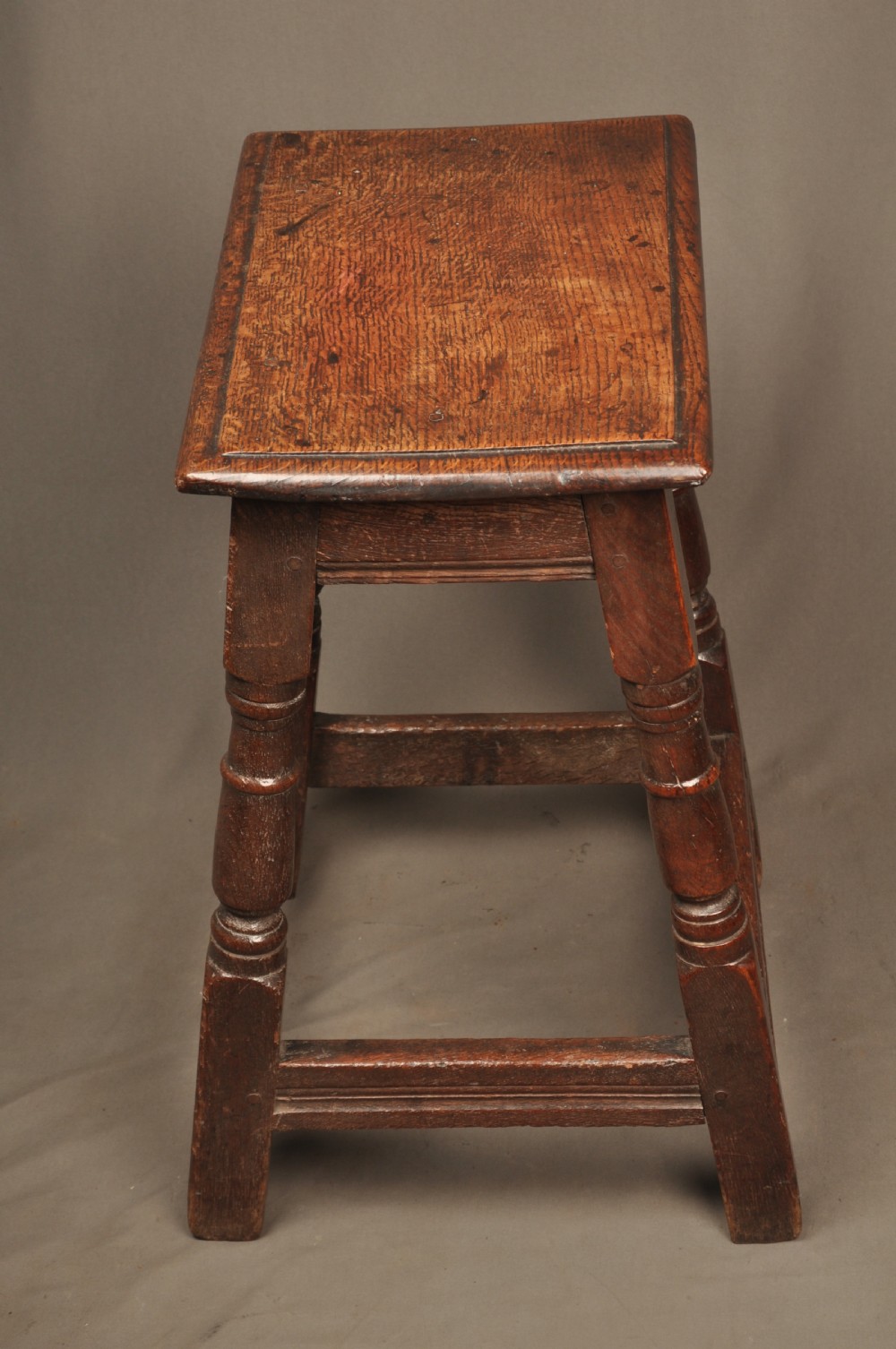 An 18th-century oak joint stool featuring baluster turned legs, plain stretchers, a rectangular moulded top, and dark brown patinated wood. View III