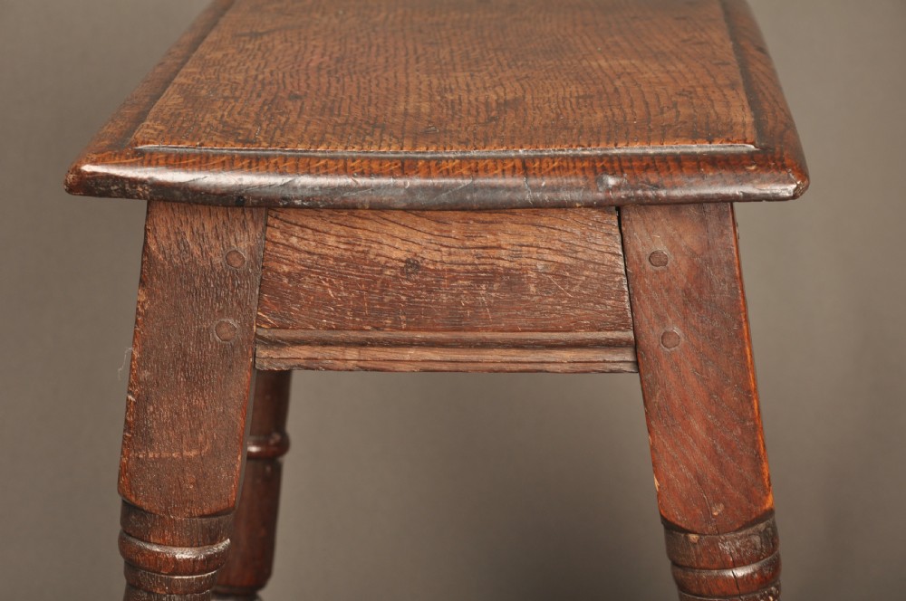An 18th-century oak joint stool featuring baluster turned legs, plain stretchers, a rectangular moulded top, and dark brown patinated wood. View V