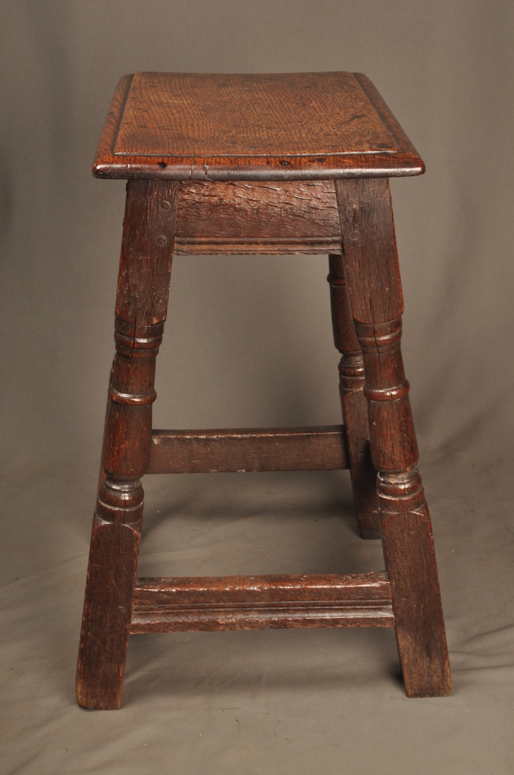 An 18th-century oak joint stool featuring baluster turned legs, plain stretchers, a rectangular moulded top, and dark brown patinated wood. View VI