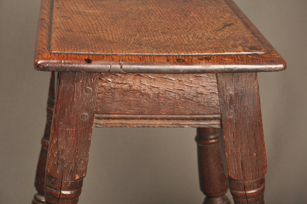 An 18th-century oak joint stool featuring baluster turned legs, plain stretchers, a rectangular moulded top, and dark brown patinated wood. View VII