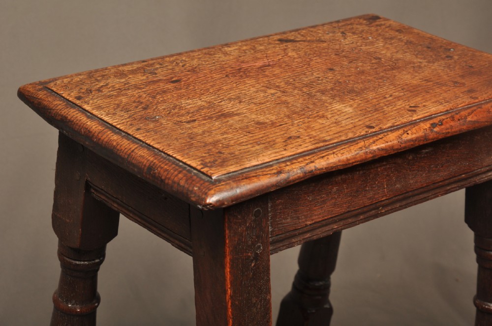 An 18th-century oak joint stool featuring baluster turned legs, plain stretchers, a rectangular moulded top, and dark brown patinated wood. View XI
