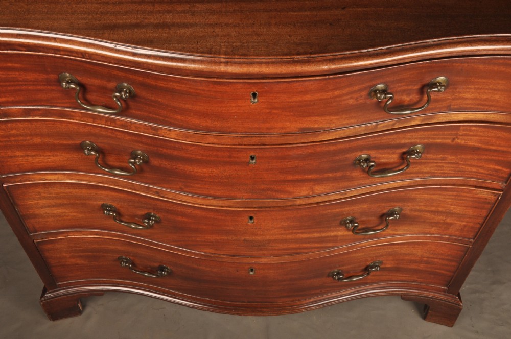 An 18th-century Georgian mahogany serpentine chest of drawers featuring four graduated drawers, brass swan-neck handles, and bracket feet. View IV