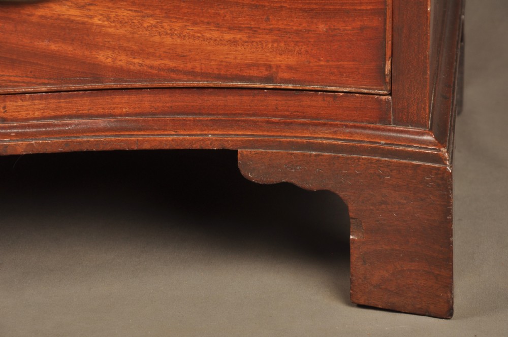 An 18th-century Georgian mahogany serpentine chest of drawers featuring four graduated drawers, brass swan-neck handles, and bracket feet. View V