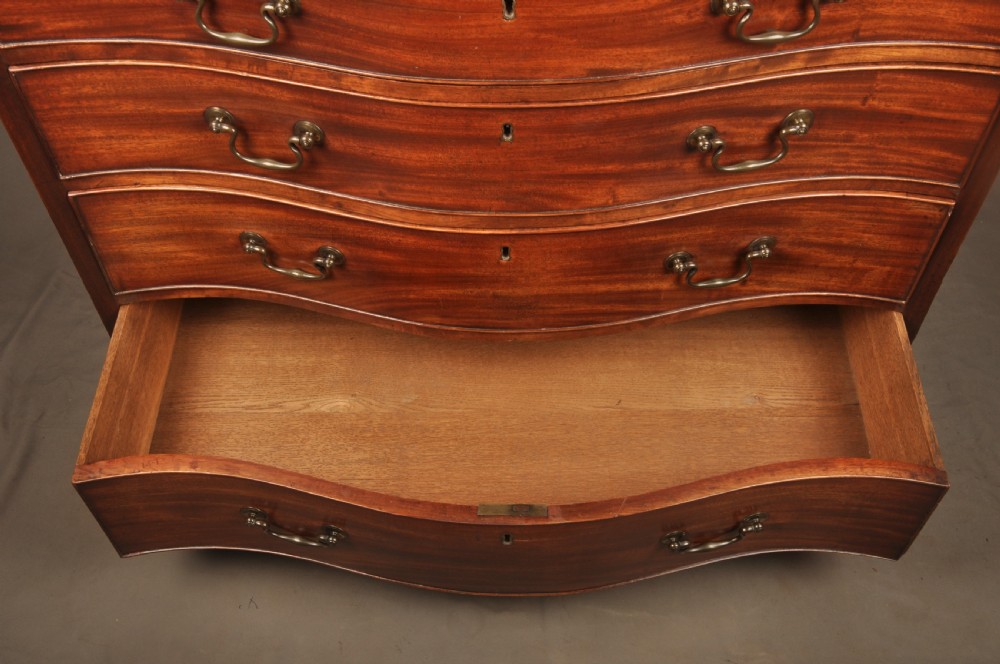 An 18th-century Georgian mahogany serpentine chest of drawers featuring four graduated drawers, brass swan-neck handles, and bracket feet. View VI