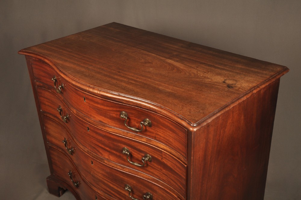 An 18th-century Georgian mahogany serpentine chest of drawers featuring four graduated drawers, brass swan-neck handles, and bracket feet. View XII