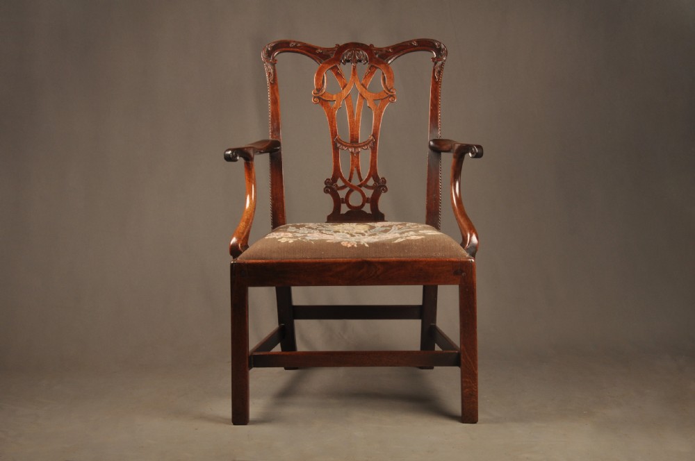 An 18th-century Georgian Chippendale mahogany armchair featuring a carved pierced splat back, shaped arms, and a floral needlepoint drop-in seat.