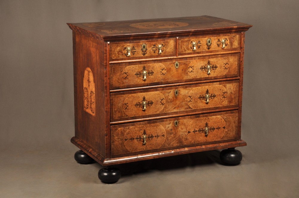 A late 17th-century walnut chest of drawers featuring arabesque marquetry inlays, tear-drop brass handles, and ebonised bun feet.