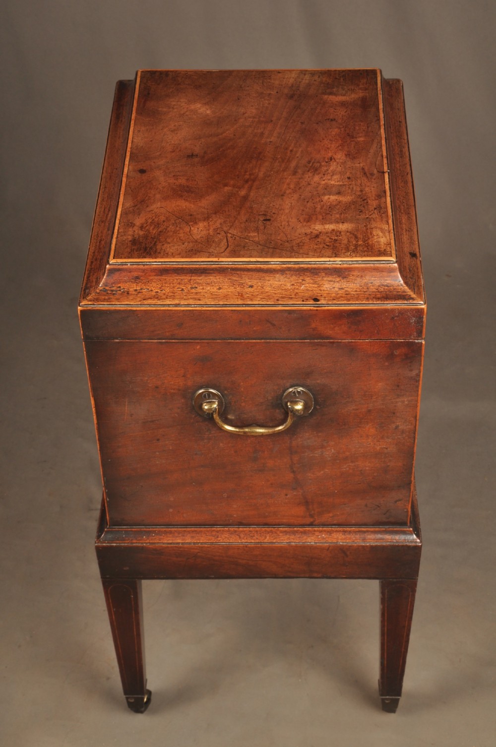 A Sheraton style mahogany cellarette featuring a hinged sarcophagus top, brass side handles, and square tapered legs on brass castors. View V