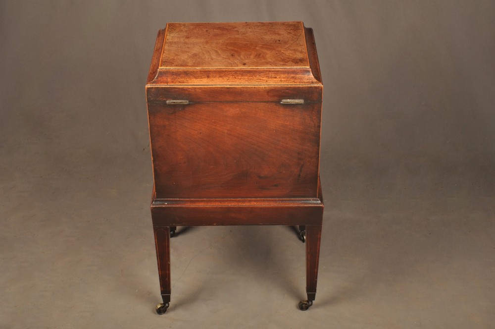 A Sheraton style mahogany cellarette featuring a hinged sarcophagus top, brass side handles, and square tapered legs on brass castors. View VI