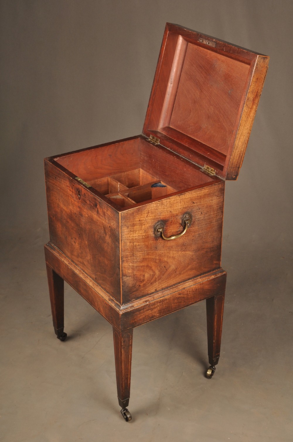 A Sheraton style mahogany cellarette featuring a hinged sarcophagus top, brass side handles, and square tapered legs on brass castors. View IX