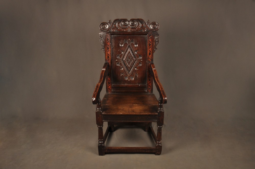 A seventeenth-century carved dark oak wainscot armchair featuring a carved lozenge motif on the back panel, scrolled cresting rail, shaped armrests, and turned front legs. View II