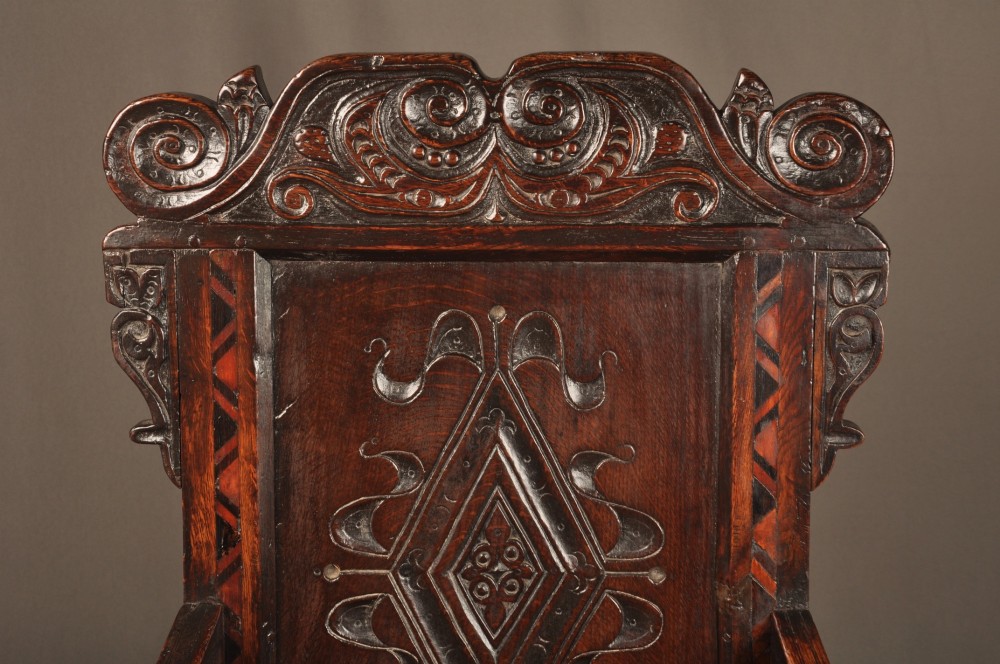 A seventeenth-century carved dark oak wainscot armchair featuring a carved lozenge motif on the back panel, scrolled cresting rail, shaped armrests, and turned front legs. View III