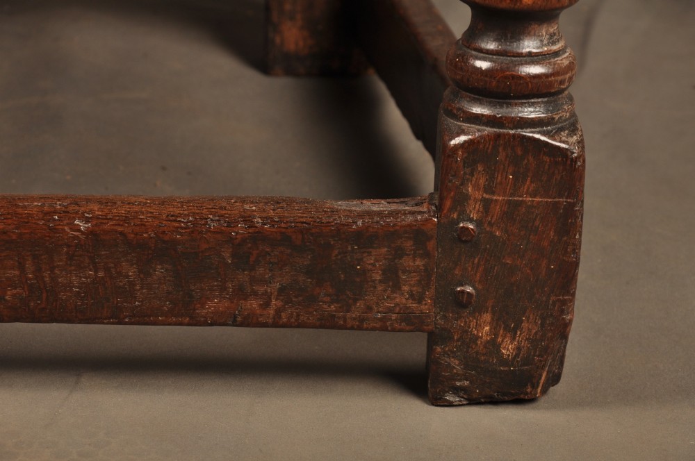 A seventeenth-century carved dark oak wainscot armchair featuring a carved lozenge motif on the back panel, scrolled cresting rail, shaped armrests, and turned front legs. View VII