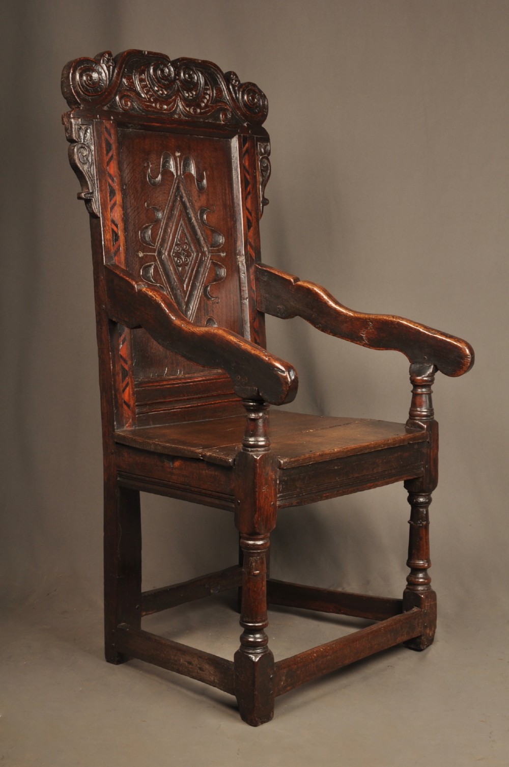 A seventeenth-century carved dark oak wainscot armchair featuring a carved lozenge motif on the back panel, scrolled cresting rail, shaped armrests, and turned front legs. View VIII