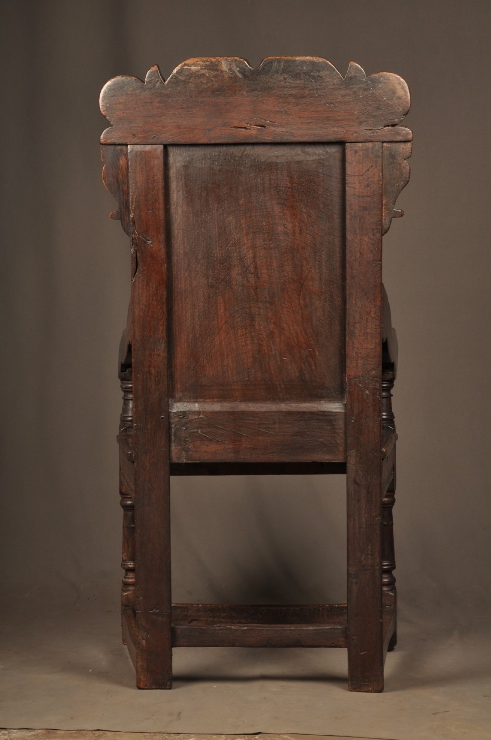 A seventeenth-century carved dark oak wainscot armchair featuring a carved lozenge motif on the back panel, scrolled cresting rail, shaped armrests, and turned front legs. View X