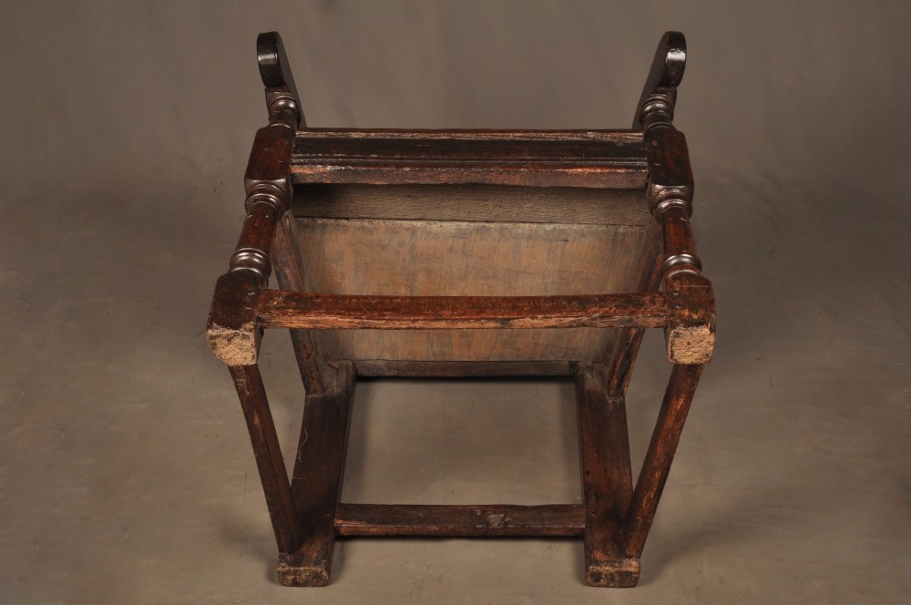 A seventeenth-century carved dark oak wainscot armchair featuring a carved lozenge motif on the back panel, scrolled cresting rail, shaped armrests, and turned front legs. View XI