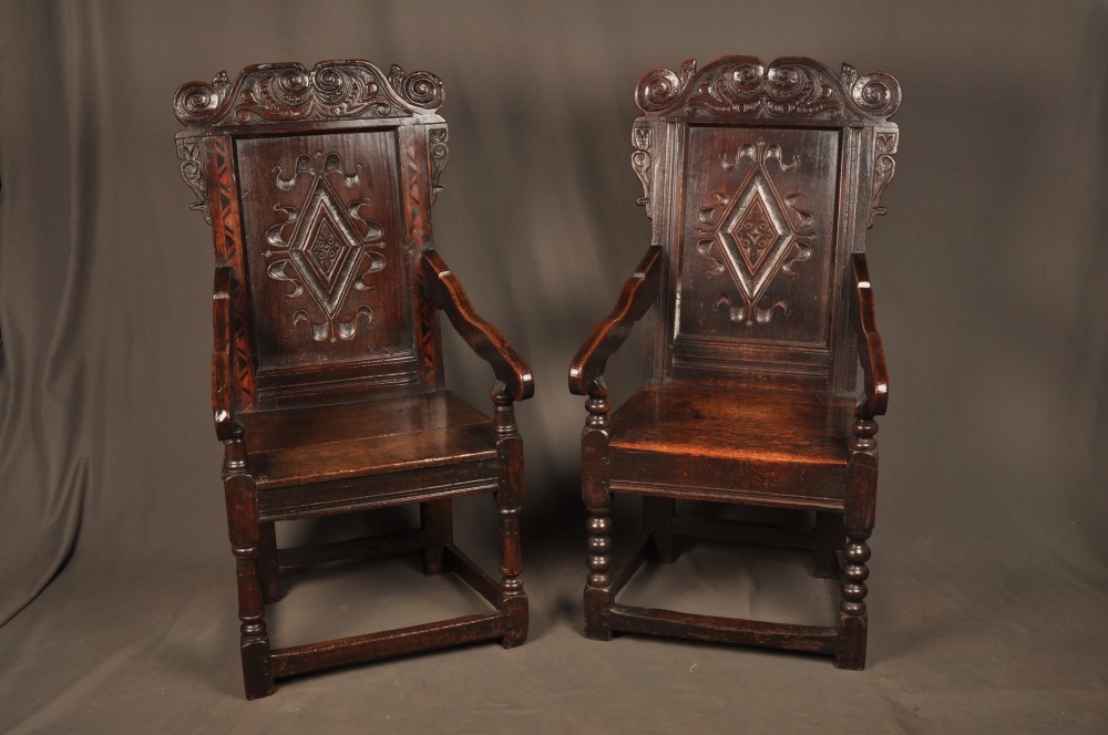 A seventeenth-century carved dark oak wainscot armchair featuring a carved lozenge motif on the back panel, scrolled cresting rail, shaped armrests, and turned front legs. View XII