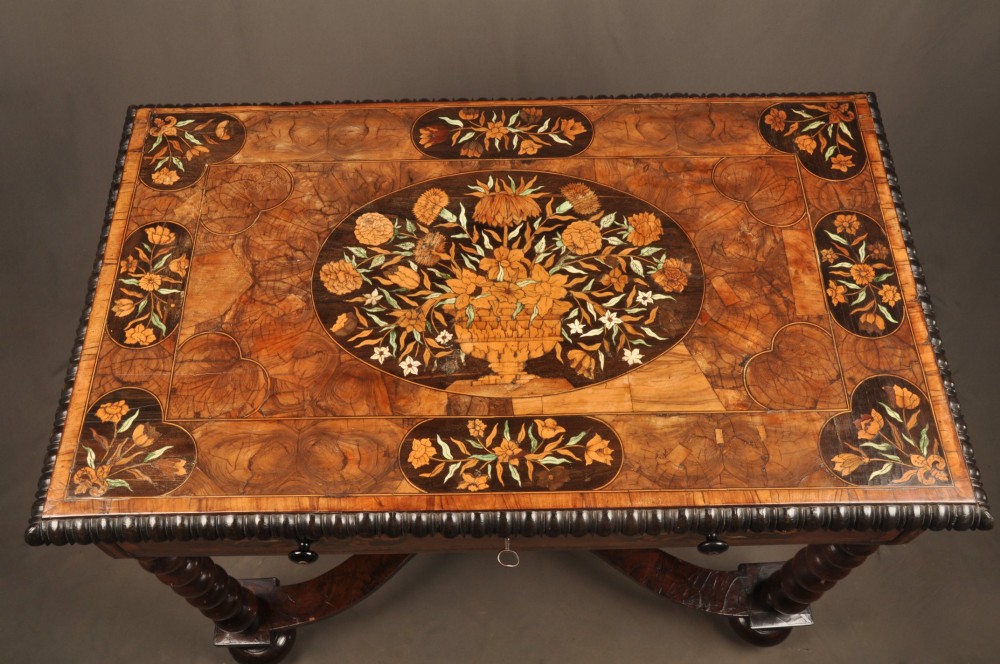 An antique brown walnut centre table featuring detailed floral marquetry inlays across the tabletop, single drawer front, and stretcher base, supported by bobbin-turned legs. View VI