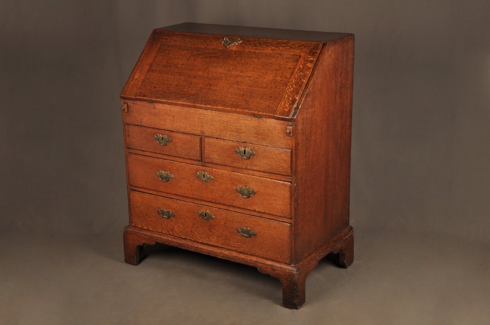 An early 18th-century oak bureau featuring a slant-front writing flap above two short and two long drawers with brass hardware.