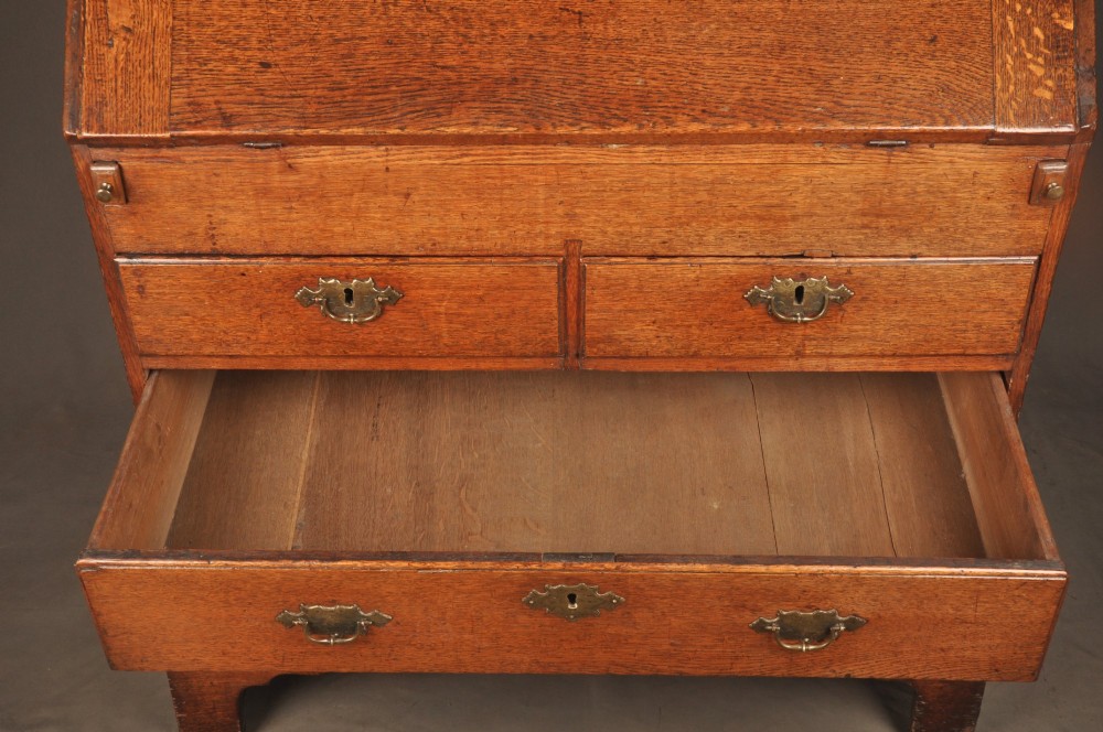 An early 18th-century oak bureau featuring a slant-front writing flap above two short and two long drawers with brass hardware. View II