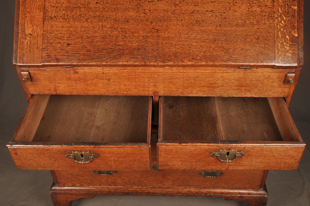 An early 18th-century oak bureau featuring a slant-front writing flap above two short and two long drawers with brass hardware. View III