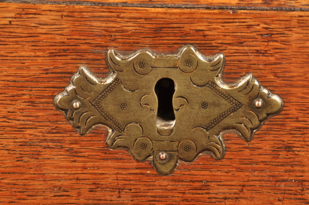 An early 18th-century oak bureau featuring a slant-front writing flap above two short and two long drawers with brass hardware. View VI