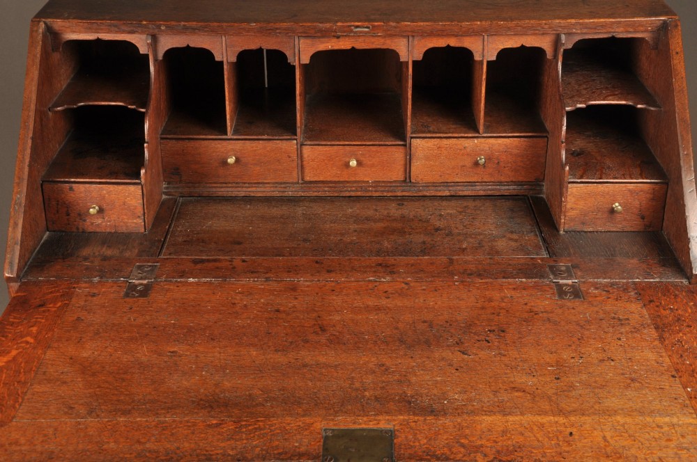 An early 18th-century oak bureau featuring a slant-front writing flap above two short and two long drawers with brass hardware. View X