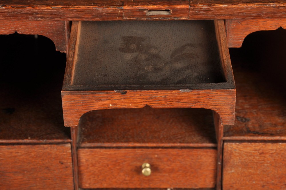 An early 18th-century oak bureau featuring a slant-front writing flap above two short and two long drawers with brass hardware. View XII