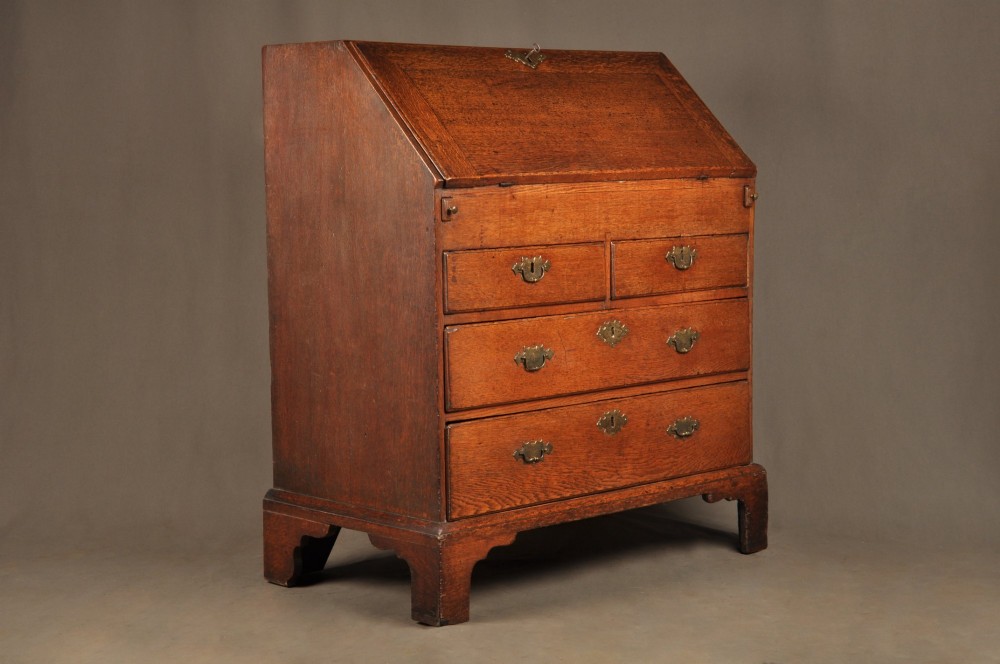 An early 18th-century oak bureau featuring a slant-front writing flap above two short and two long drawers with brass hardware. View XIII