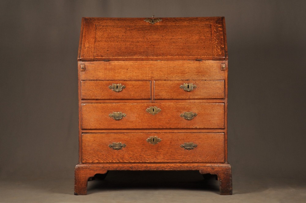 An early 18th-century oak bureau featuring a slant-front writing flap above two short and two long drawers with brass hardware. View XIV