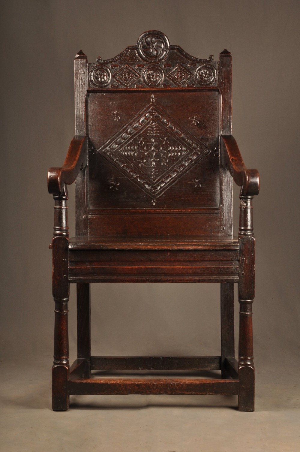 A 17th-century dark oak wainscot armchair featuring a carved lozenge back panel, turned front supports, and shaped armrests.