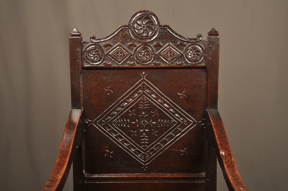 A 17th-century dark oak wainscot armchair featuring a carved lozenge back panel, turned front supports, and shaped armrests. View II
