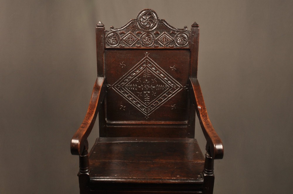 A 17th-century dark oak wainscot armchair featuring a carved lozenge back panel, turned front supports, and shaped armrests. View III