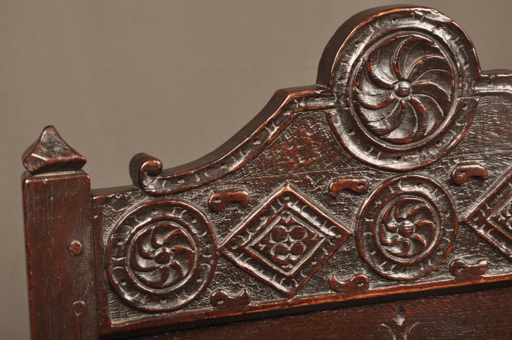 A 17th-century dark oak wainscot armchair featuring a carved lozenge back panel, turned front supports, and shaped armrests. View V
