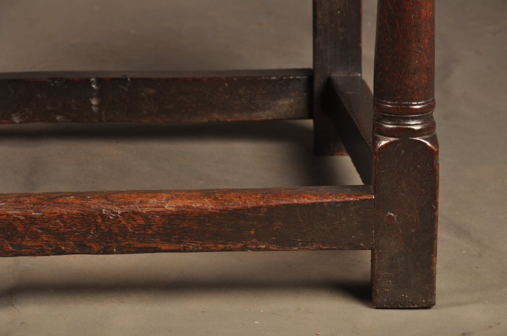 A 17th-century dark oak wainscot armchair featuring a carved lozenge back panel, turned front supports, and shaped armrests. View VI